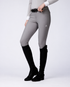 A model wearing light gray equestrian riding breeches with a subtle textured pattern on the thigh, paired with black riding boots and a white long-sleeve shirt, shown from the waist down against a light gray studio background.