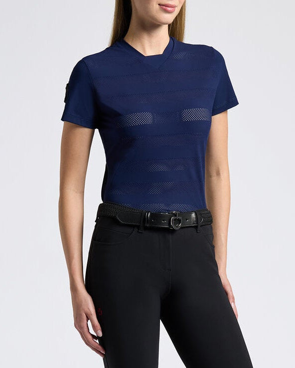 A woman modeling a navy blue short-sleeve athletic top and black riding breeches with black riding boots, standing against a light gray studio background.