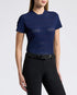 A woman modeling a navy blue short-sleeve athletic top and black riding breeches with black riding boots, standing against a light gray studio background.